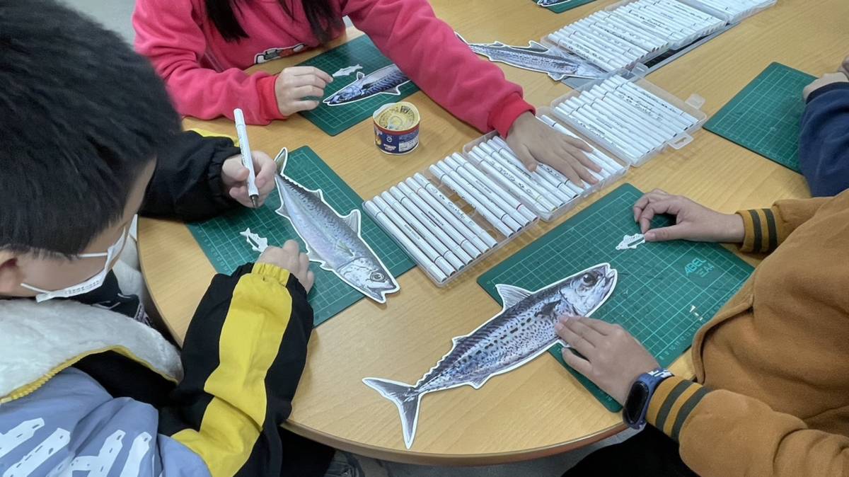 港西國小食魚課堂上，同學們透過圖卡、紙模型認識鯖魚，學習鯖魚品種、產地和產季，了解鯖魚加工製作成罐頭的流程。