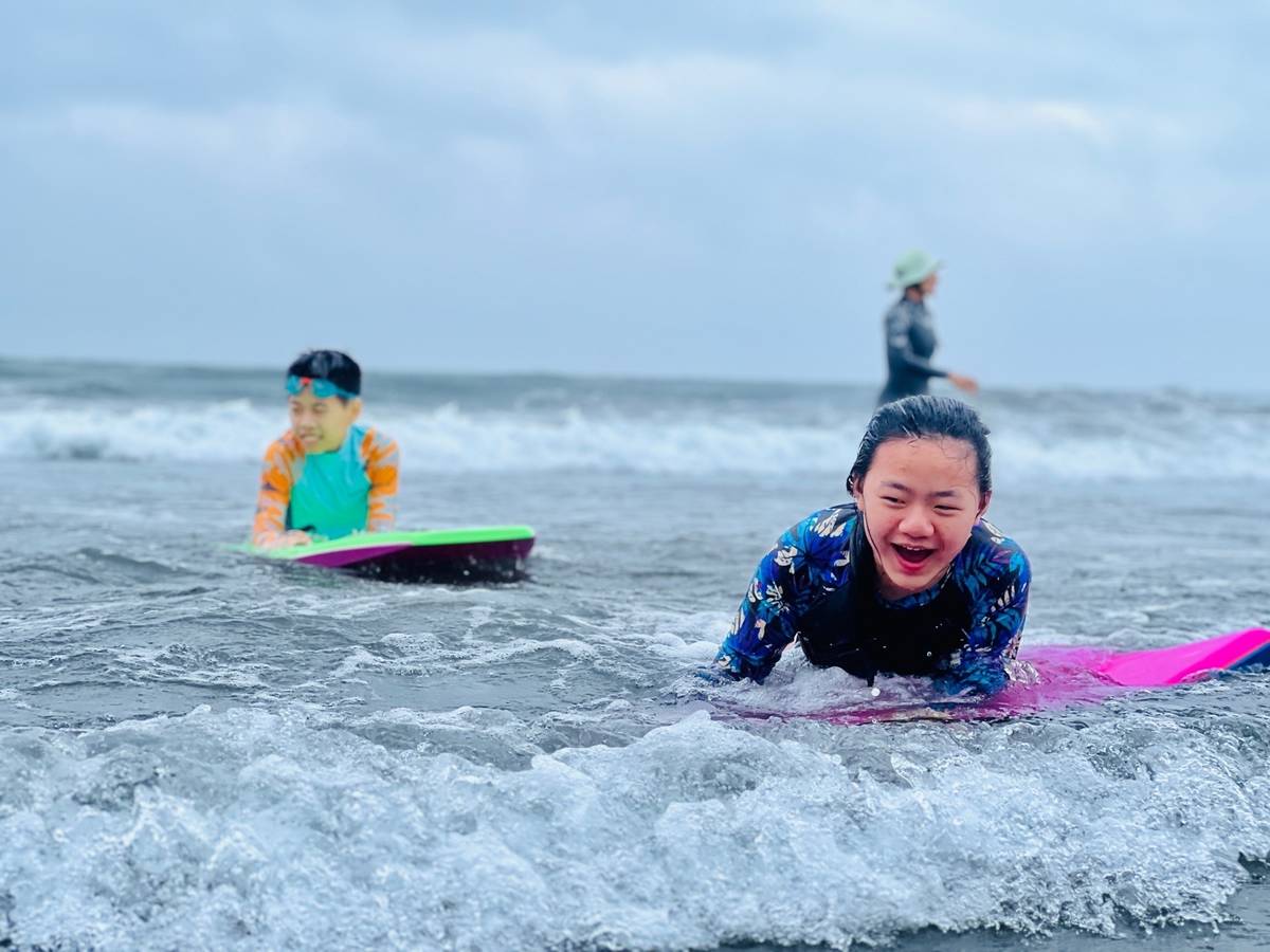 學生趴向浪板，享受被海水用力沖上岸的樂趣