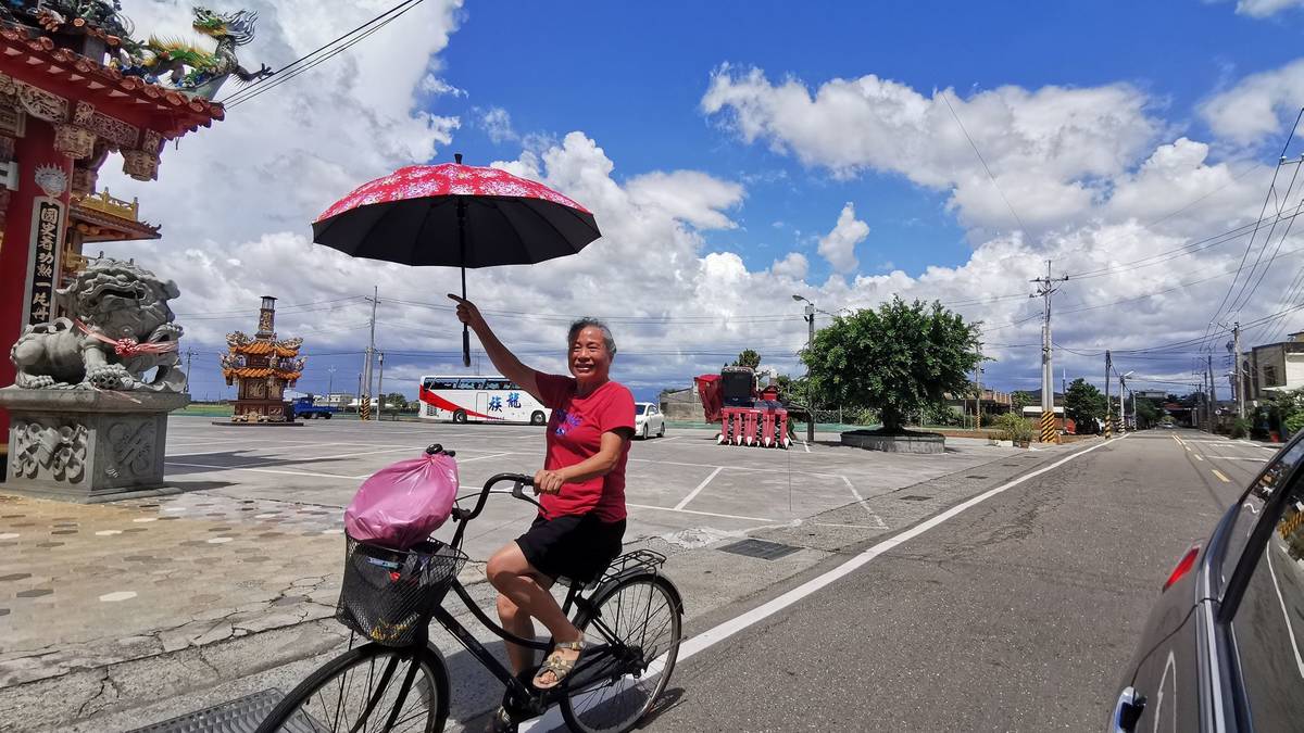 廖寶粟手持客家花布傘，騎腳踏車在溪口鄉柴林村