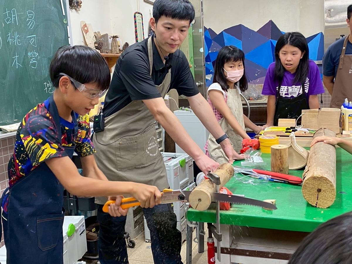 北科大、政大實小合作「城市蜂巢」木工營隊，協助學童安全操作折合鋸，將木材依需求鋸切。(北科大提供)