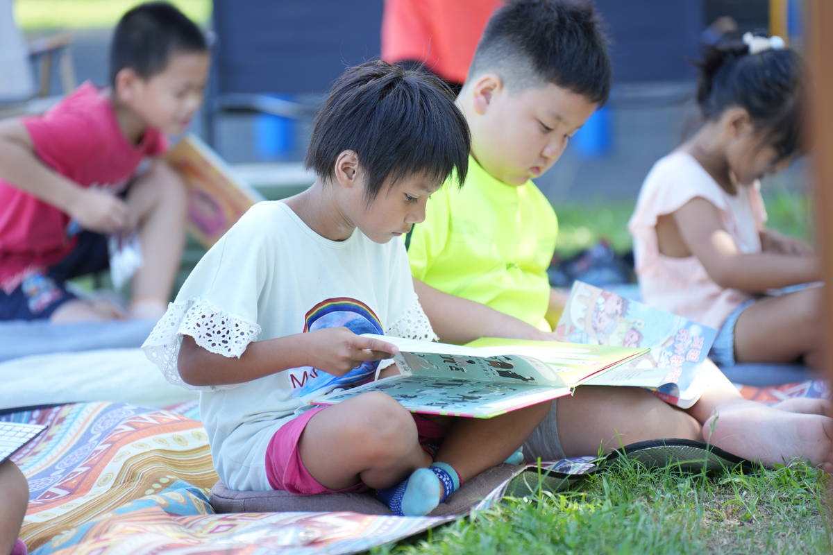 人權故事車前進校園，學童挑選書籍後，坐在草地上專注閱讀。(人權館提供)