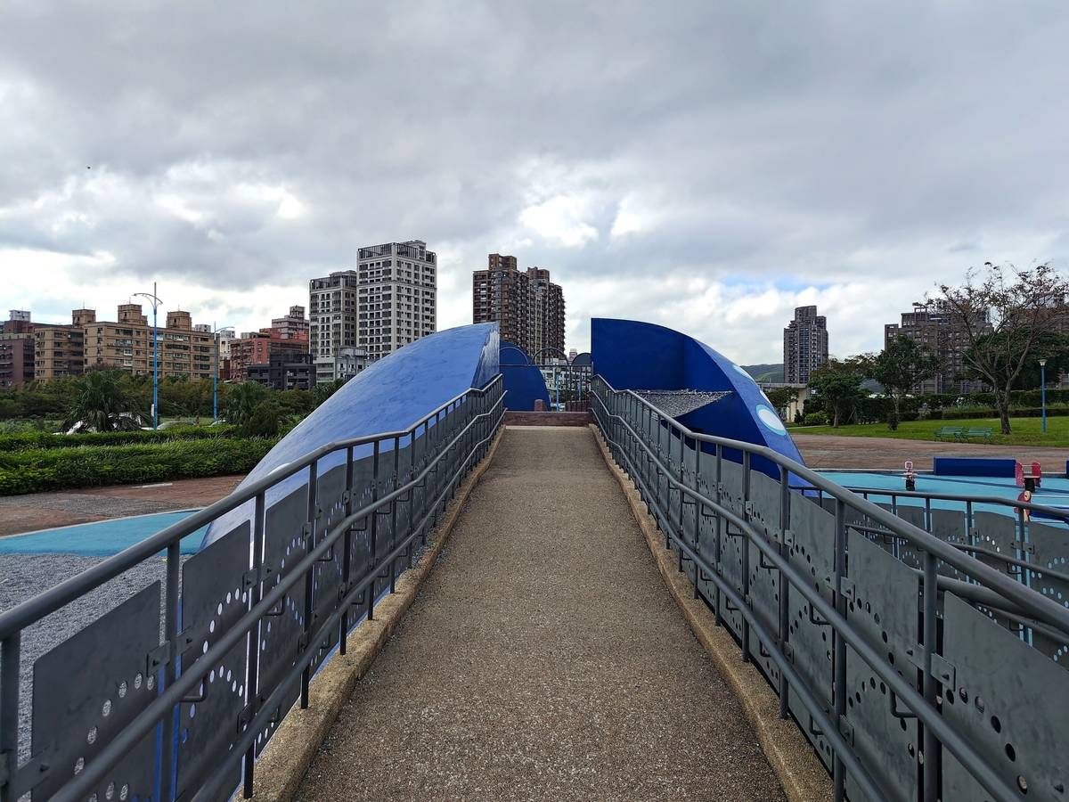 八里區商港公園鯨魚造型溜滑梯，左右兩側分別以攀爬梯及無障礙坡道提供不同遊戲路徑