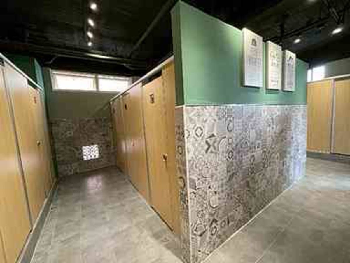 中正國中女廁以木紋隔間與墨綠主牆呈現沈穩調性，搭配灰階花磚增添層次與美感